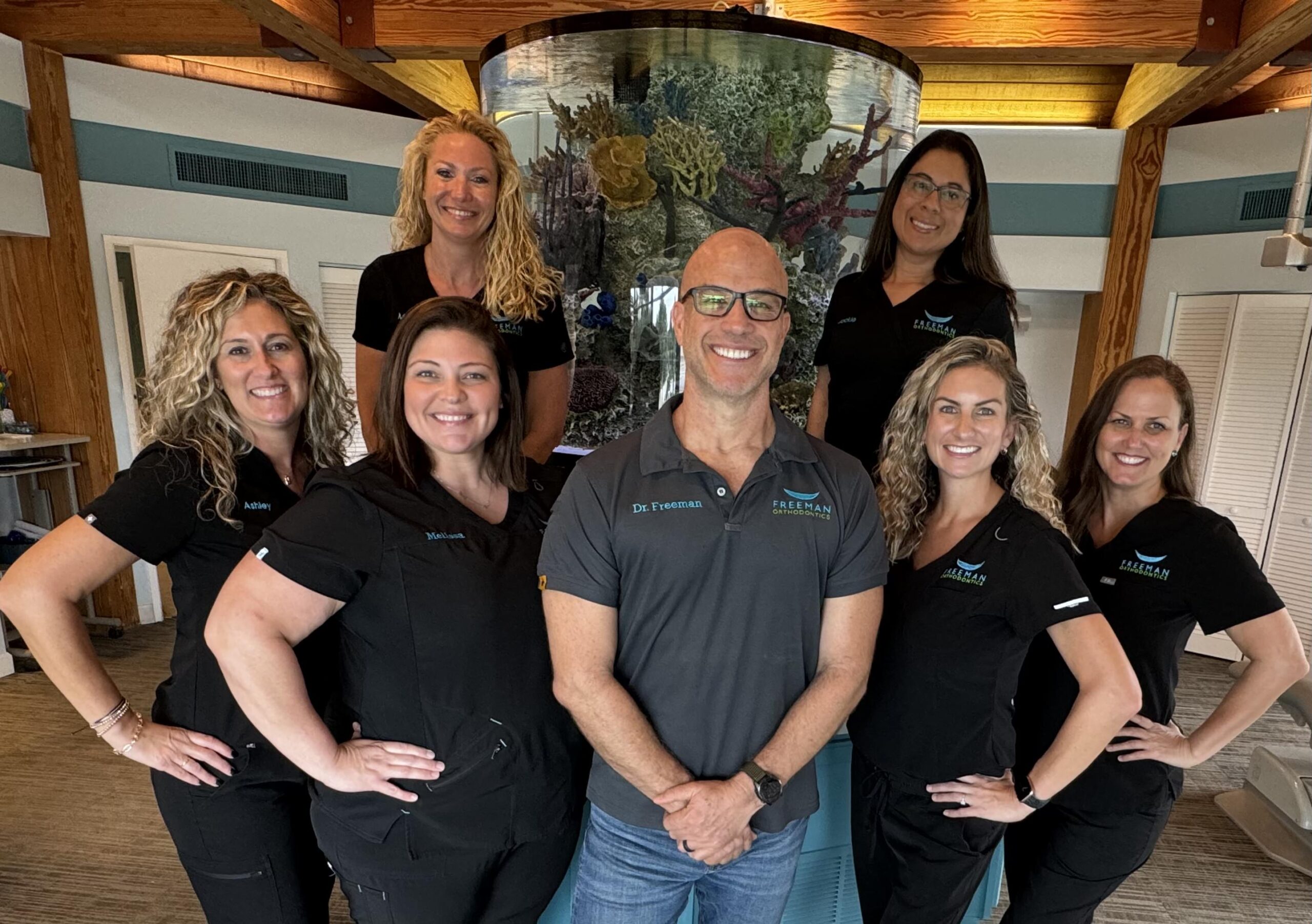 Group photo of Dr. Freeman and the orthodontic team at Freeman Orthodontics, smiling and posing together in front of a vibrant aquarium in their office.